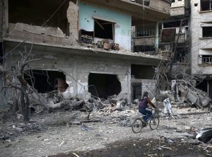 A young boy rides a bicycle, near damaged houses, after an air raid in the besieged town of Douma, Eastern Ghouta, Damascus, Syria February 23.