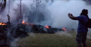 A man wearing a gas mask takes pictures of a lava fissure in Leilani Estates, Hawaii, U.S. May 9, 2018, in this still image taken from a social media video. Apau Hawaii Tours/Social Media via REUTERS