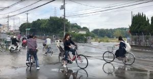 People cycle on a flooded road damaged after an earthquake hit Osaka, Japan June 18, 2018, in this still image taken from a video obtained from social media. MANDATORY CREDIT. Twitter/@tw_hds/via REUTERS