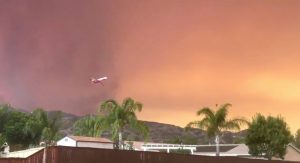 A plane flies off after dumping fire retardant over the Holy Fire close to a residential area in Lake Elsinore, California, the U.S. August 8, 2018 in this still image taken from a video obtained from social media. Camille Collins/via REUTERS