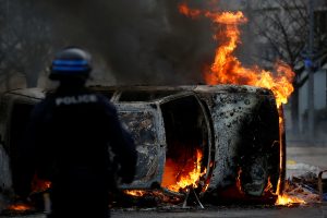 A French riot policeman stands next to a burning car as youth and high school students protest against the French government's reform plan, in Nantes, France, December 6, 2018. REUTERS/Stephane Mahe